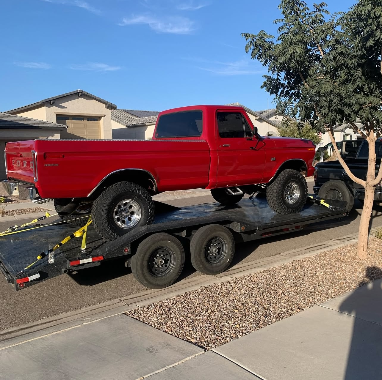 20ft flatbed trailer with drive-over fenders transporting a red pickup truck in Albuquerque